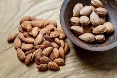 Ahşap bir arka planda ahşap bir kasede soyulmuş badem ve badem kabuğu. Fındık, beslenme ve çiğ gıda konsepti