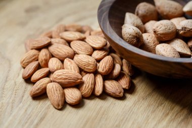 Ahşap bir arka planda ahşap bir kasede soyulmuş badem ve badem kabuğu. Fındık, beslenme ve çiğ gıda konsepti