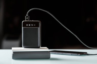 Siyah bir güç bankası ve siyah kabloyla çalışan akıllı telefon yığını. Ekstra güç kaynağı. Asgari promosyon imajı  