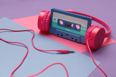 Pembe kulaklıklar ve parlak pembe, mor ve mavi renkli arka planda mavi bant ses kaseti. Audiophile müzik konsepti
