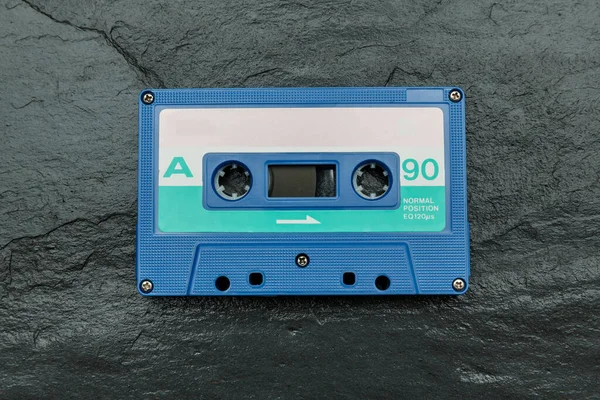 Blue tape audio cassette on a wet slate stone background.
