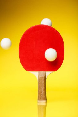 Ping pong raketinin kırmızı tarafı. Havada üç beyaz top var. Sarı arka planda duruyor. Table tenis ping pong yarışması konsepti.