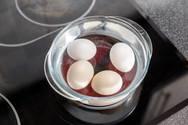 Elektrikli ocağın üstünde cam bir tencerede suda yumurta. Haşlanmış yumurta.