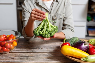 Mutfak arka planında brokoli tutan kadın eller ve farklı sebzeler. Sağlıklı yemek pişirme konsepti