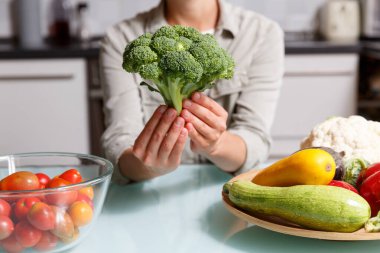Mutfak arka planında brokoli tutan kadın eller ve farklı sebzeler. Sağlıklı yemek pişirme konsepti