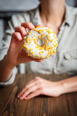 Beyaz jöleli donut tutan kadın elleri ve sarı şekerleme serpintileri. Tatlılar, kekler ve çörekler 
