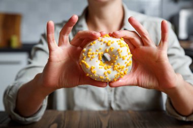 Beyaz jöleli donut tutan kadın elleri ve sarı şekerleme serpintileri. Tatlılar, kekler ve çörekler 