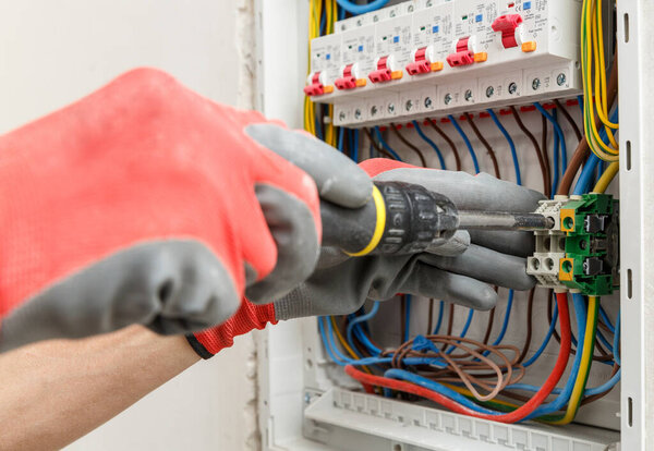 Close up of electrician's hands in working gloves installing and maintainin electrical junction box. Electrical services concept  