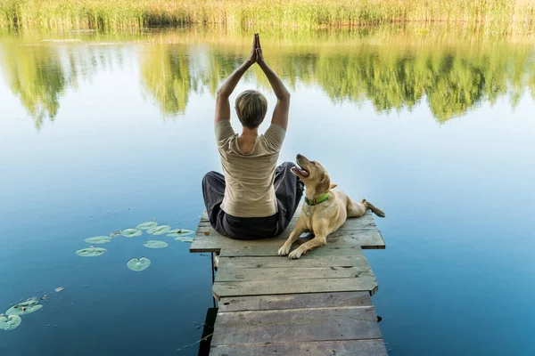 Female with a labrador dog on a wooden fishing bridge exercising and enjoying peaceful warm water view. Relaxatioan and spare time with home pets.