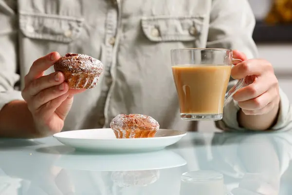 close up of right hand taking one of two curd muffins from plate, and left hand holding glass cup of coffee with milk. Delicious and aroma snack
