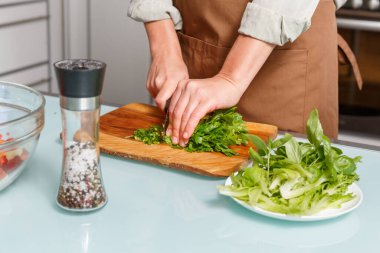 Ahşap bir tahtanın üzerinde salata için sebze kesen kadın eller mutfağın arka planına karşı. Sağlıklı yemek pişirme konsepti