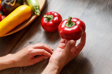 Ahşap arka planda tatlı dolmalık biber tutan kadın elleri ve farklı sebzeler. Sağlıklı yemek pişirme konsepti