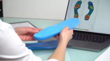Dişi ortopedist, elinde özel yapım tabanlar bulunan bir klinikte dizüstü bilgisayarın önünde, üzerinde test ayakları resmi olan bir kadın ortopedist. Ayakların dinlenmesi ve ortotik tıp konsepti