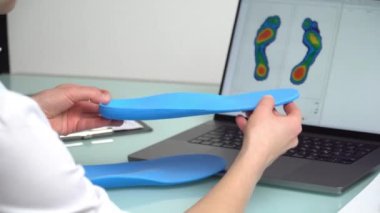 Dişi ortopedist, elinde özel yapım tabanlar bulunan bir klinikte dizüstü bilgisayarın önünde, üzerinde test ayakları resmi olan bir kadın ortopedist. Ayakların dinlenmesi ve ortotik tıp konsepti