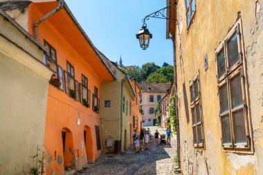 SIGHISOARA, ROMANIA - 8 Ağustos 2019: UNESCO tarafından dünya mirası olarak listelenen Romanya 'nın Sighisoara kentindeki eski ortaçağ sokaklarında yürüyen insanlar