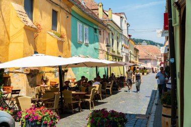 SIGHISOARA, ROMANIA - 8 Ağustos 2019: UNESCO tarafından dünya mirası olarak listelenen Romanya 'nın Sighisoara kentinde sokak kafeleri bulunan Octavian Goga caddesi