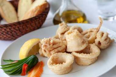 Akdeniz restoranında beyaz bir tabakta servis edilen hamur içinde kızarmış mürekkep balığını yakından çek. Akdeniz mutfağının bir parçası olarak deniz ürünleri