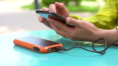 4k görüntüsü, taşınabilir güç bankasıyla şarj edilirken cep telefonu kullanan bir kadının elleri. Enerji tasarrufu teknolojisi