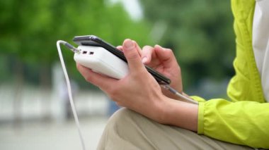 Beyaz enerji bankasıyla şarj ederken cep telefonu kullanan kadın eller. Yavaş çekim. Enerji tasarrufu teknolojisi