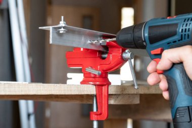 Matkap olarak kullanılan elektrikli tornavidayla erkek eli, çilingir mengenesine alüminyum detaylarda delikler açıyor. Ev onarım konsepti