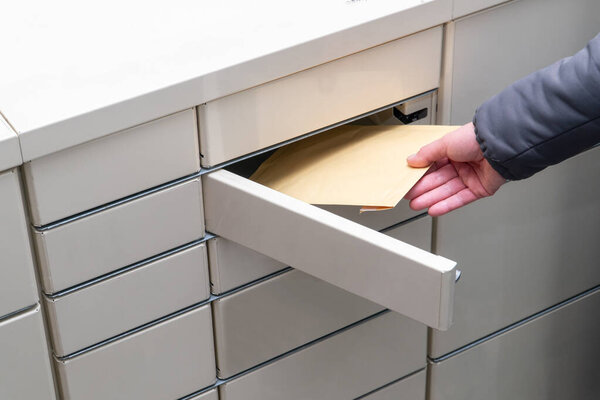 Female hand puts an envelope in a post terminal machine.  Parcel delivery concept
