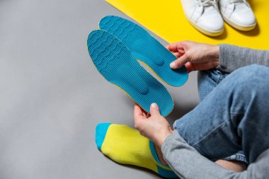 Mavi ortopedik taban tutan kadın elleri, gri arka planda beyaz spor ayakkabılar. Sağlık ve ortopedik tedavi ve yassı ayak kavramının önlenmesi. 