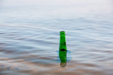 Nehirde yüzen yeşil cam bir şişe, su yüzeyinde darboğaz görünüyor. Çevre koruma ve atık kontrol kavramı.