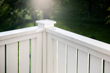 Beyaz tırabzanlar, saksılar, mobilyalar ve manzara manzarası olan ahşap yürüyüş güvertesi.