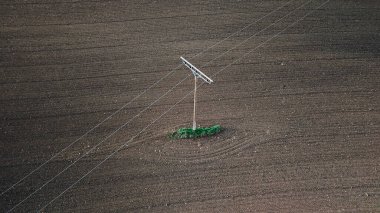 Elektrikli bir direğin minimalist bir görüntüsü tarlada, sadelik ve kontrastlık sergiliyor. Temiz çizgiler ve açık alan huzurlu ve sanatsal kırsal bir manzara yaratır..