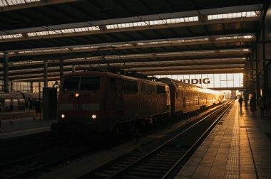 Sanayi mimarisi ve metal çatılı Münih Merkez İstasyonu 'nun (Hauptbahnhof) içi. Atmosferik düşük ışıklandırmada platformları ve demiryolu altyapısını gösteren uzun perspektif.