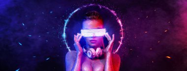 Gözlüklü ve kulaklıklı neon ışıklı kız DJ. Yüzünde ve vücudunda menekşe rengi boyalı güzel bir kadın. Kulüp partisinde seksi TDJ portresi