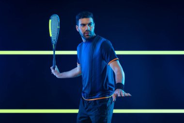 Squash oyuncusu raketle squash sahasında. Sahada raketli, neon renkli bir erkek sporcu. Spor konsepti. Bir spor uygulaması ya da bahis sitesi tasarımı için yüksek kaliteli bir fotoğraf indir