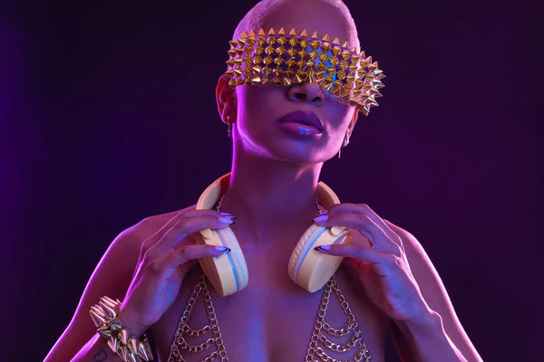 Girl DJ in neon lights with glasses and headphones. Beautiful woman in violet paint on her face and body. Portrait of sexy TDJ at club party