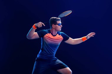 Spor kıyafetli Badminton oyuncusu raket salıncağıyla mekiğe uzanıyor. Stüdyo çekimi.