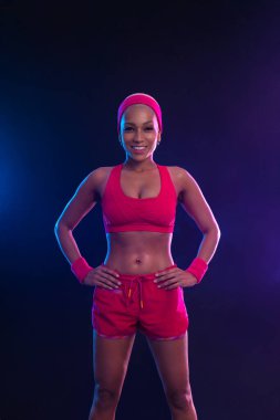 Sportif formda bir kadın, dambılı bir atlet siyah arka planda spor yapıyor. Beden eğitimi dersleri için müzik koleksiyonunu indir. Spor eğlencesi. Güzel siyah genç kadın.