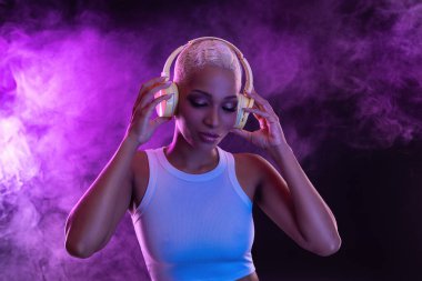 Hippi moda kızı, Afro-Amerikan modeli kulaklık takıyor ve yeni havalı müzik karışımının keyfini çıkarıyor. Mor stüdyo arka planında Mor kulüp mor parti ışığıyla sisli bir kadın.