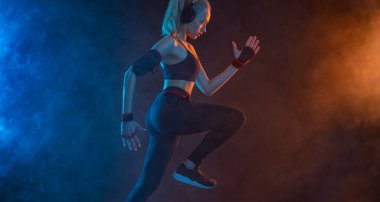 Koşucu kaçıyor. Hızlı koşu. Siyah arka planda koşan güçlü atletik kadın spor giyim kuşamında neon ışıklar takıyor. Spor ve spor motivasyonu