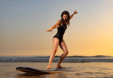 Uzun saçlı sörfçü kız sörfe gider. Gün batımında ya da gün doğumunda sahilde sörf tahtası tutan bir kadın. Sörfçü ve okyanus.
