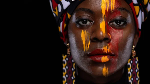 Yellow and red body paint. Woman with face art. Young girl with bodypaint. An amazing African model with makeup. Close-up