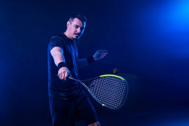 Squash oyuncusu raketle squash sahasında. Sahada raketli, neon renkli bir erkek sporcu. Spor konsepti. Bir spor uygulaması ya da bahis sitesi tasarımı için yüksek kaliteli bir fotoğraf indir