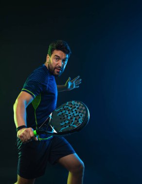 Raketli Padel tenisçi. Sahada raketli, neon renkli bir erkek sporcu. Spor konsepti. Bir spor uygulaması ya da bahis sitesi tasarımı için yüksek kaliteli bir fotoğraf indir