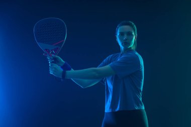 Raketli Padel tenisçi. Sahada raketi neon renkli genç bir sporcu kız. Spor konsepti. Bir spor uygulaması ya da bahis sitesi tasarımı için yüksek kaliteli bir fotoğraf indir