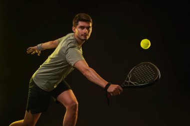 Raketli Padel tenisçi. Sahada raketli, neon renkli bir erkek sporcu. Spor konsepti. Bir spor uygulaması ya da bahis sitesi tasarımı için yüksek kaliteli bir fotoğraf indir