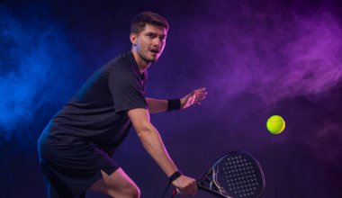 Raketli Padel tenisçi. Sahada raketli, neon renkli bir erkek sporcu. Spor konsepti. Bir spor uygulaması ya da bahis sitesi tasarımı için yüksek kaliteli bir fotoğraf indir