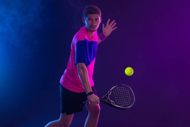 Raketli Padel tenisçi. Sahada raketli, neon renkli bir erkek sporcu. Spor konsepti. Bir spor uygulaması ya da bahis sitesi tasarımı için yüksek kaliteli bir fotoğraf indir