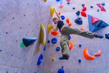 Kaya tırmanışı yapan kadın sporcu. Spor salonundaki kaya tırmanışında antrenman yapıyor. Duvara tırmanıyor. Genç, formda bir kız ekstrem spor hobisinde eğleniyor. Yüksek çözünürlüklü fotoğraf