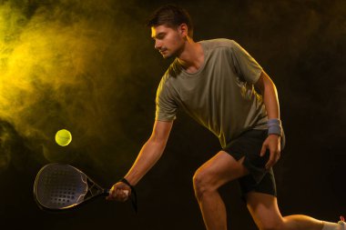 Raketli Padel tenisçi. Sahada raketli, neon renkli bir erkek sporcu. Spor konsepti. Bir spor uygulaması ya da bahis sitesi tasarımı için yüksek kaliteli bir fotoğraf indir