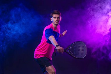 Raketli Padel tenisçi. Sahada raketli, neon renkli bir erkek sporcu. Spor konsepti. Bir spor uygulaması ya da bahis sitesi tasarımı için yüksek kaliteli bir fotoğraf indir