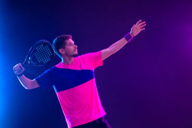 Raketli Padel tenisçi. Sahada raketli, neon renkli bir erkek sporcu. Spor konsepti. Bir spor uygulaması ya da bahis sitesi tasarımı için yüksek kaliteli bir fotoğraf indir