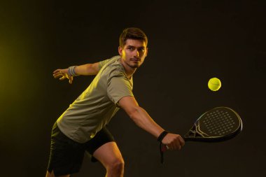 Raketli Padel tenisçi. Sahada raketli, neon renkli bir erkek sporcu. Spor konsepti. Bir spor uygulaması ya da bahis sitesi tasarımı için yüksek kaliteli bir fotoğraf indir